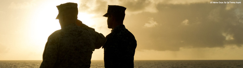 Two Marines looking out onto the water in front of sunset.